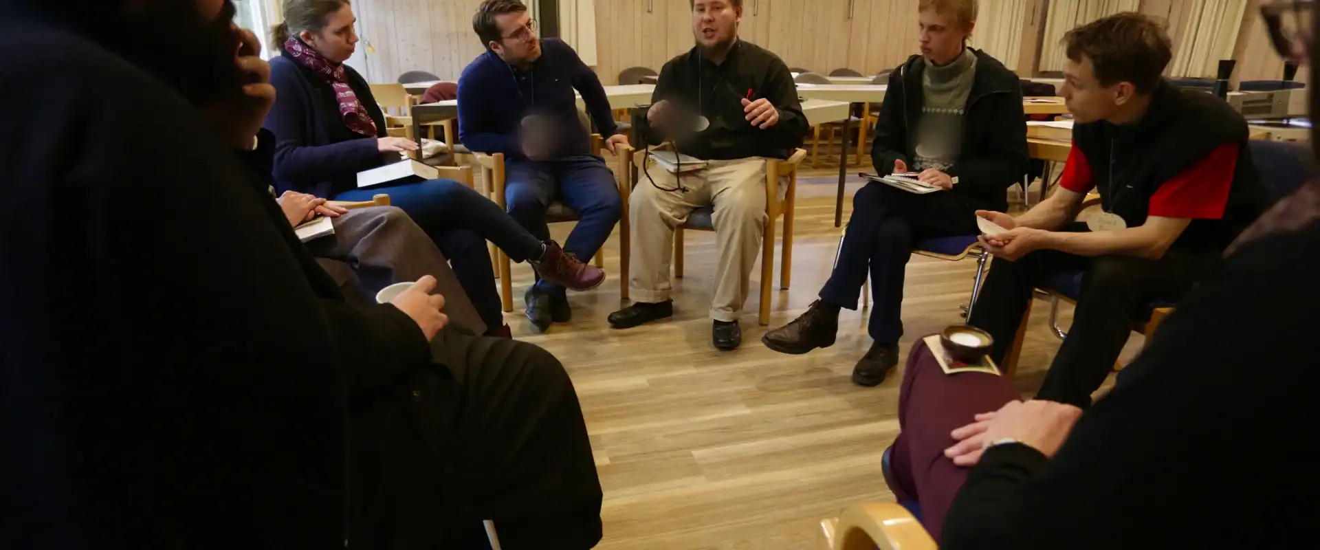 Eine Gruppe von etwa zehn Menschen sitzt im Stuhlkreis in einem hellen Raum mit Holzboden und spricht miteinander.