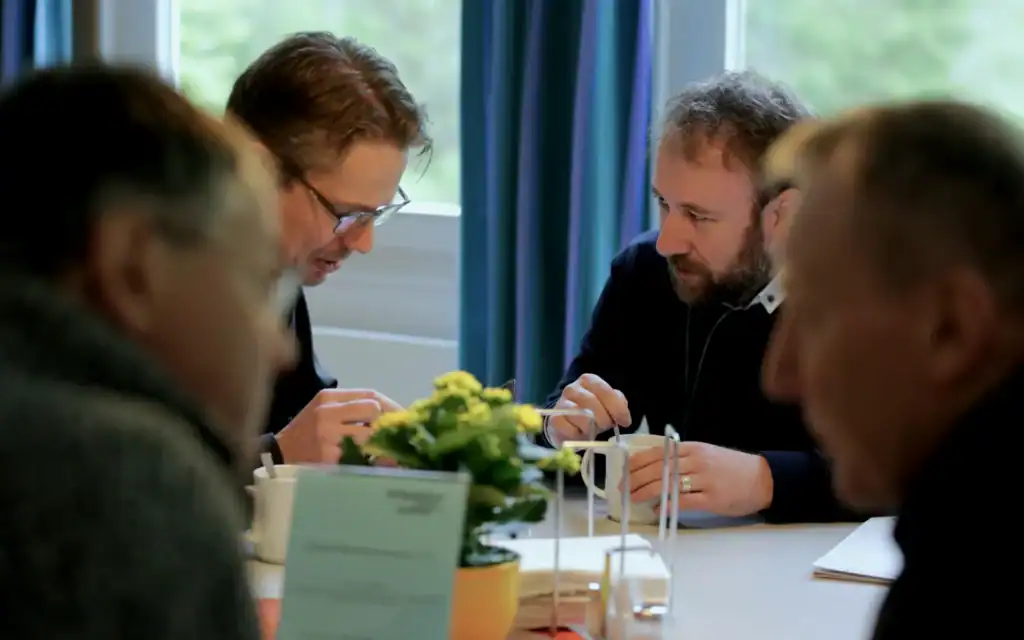 Vier Menschen sitzen an einem Tisch, vor ihnen liegen Papiere und Unterlagen, sie arbeiten konzentriert.